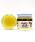 A small open jar of yellow salve with a blue lid, next to its packaging that reads 'Calendula Salve' with additional text indicating organic herbal skin care.